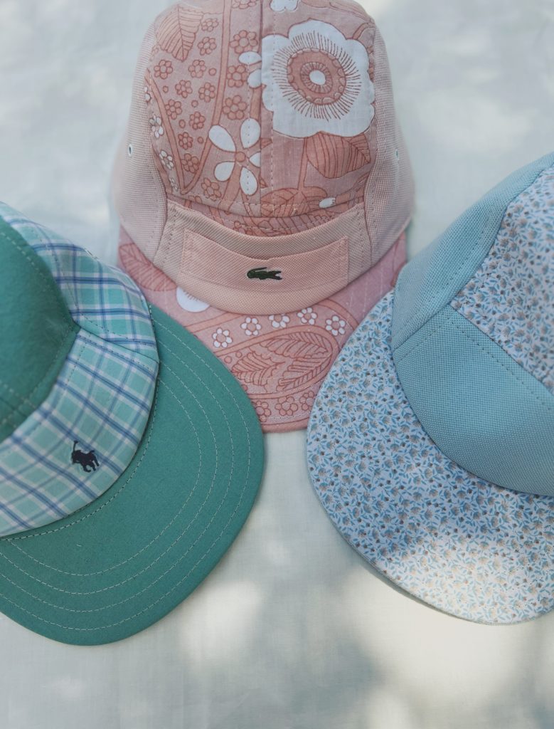 IMG_6394 Upcycling de casquettes. Casquettes upcyclées, de couleur verte, rose, et bleu, aux motifs fleuris. Disposées en forme de triangle sur un fond blanc.